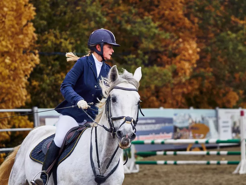 Young woman jockey in white blue dress and black boots, takes part in equestrian competitions. Close-up.