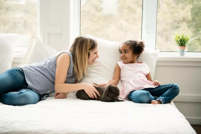 A little girl and her mom petting a bunny on the bed