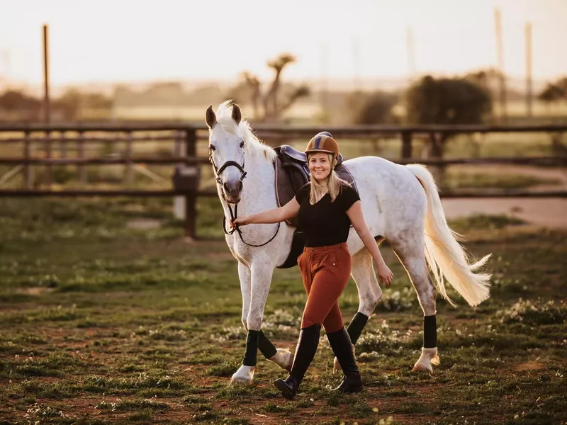 Blond young girl walking with her white mare